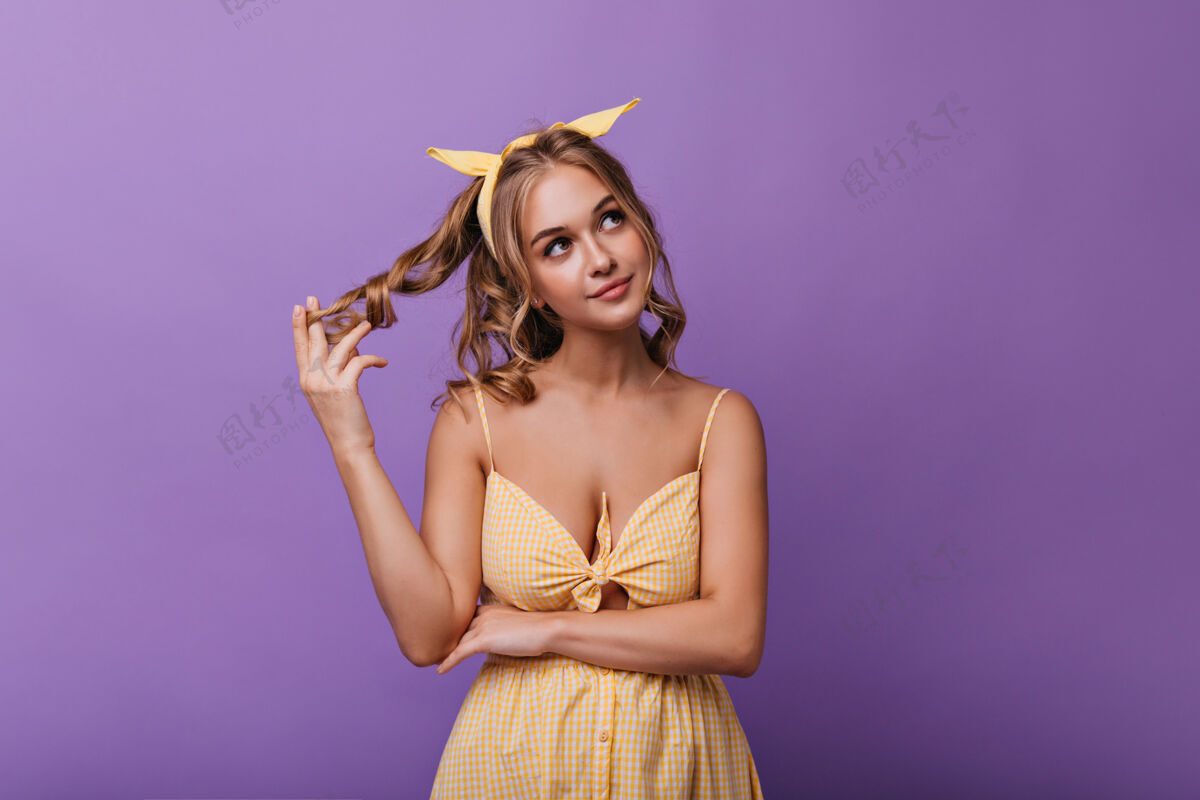乐趣嬉戏着金色卷发的快乐沉思的女孩穿着黄色连衣裙站在紫色地上的性感晒黑的女人休闲积极模特