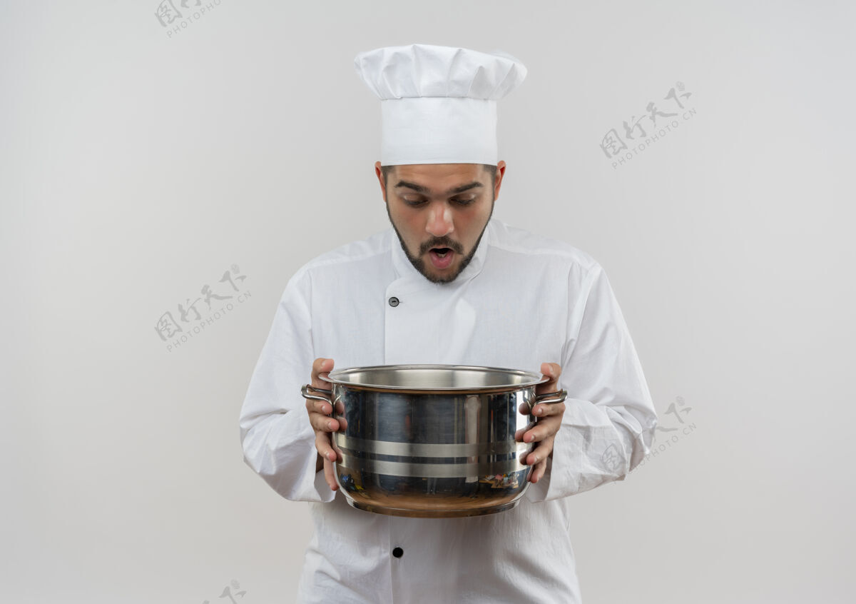 拿着惊讶的年轻男厨师穿着厨师制服 拿着锅看里面的白色空间隔离看制服里面