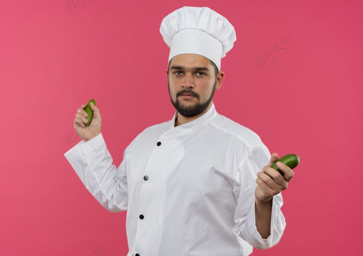 抱着年轻的男厨师穿着厨师制服 手里拿着黄瓜 在粉红色的空间里显得与世隔绝厨师粉红男