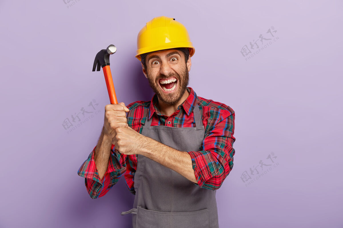车间绝望的男工或修理工双手持榔头 表情暴躁 准备修理或建造 戴防护帽 在工地工作 站在室内修理室内设备
