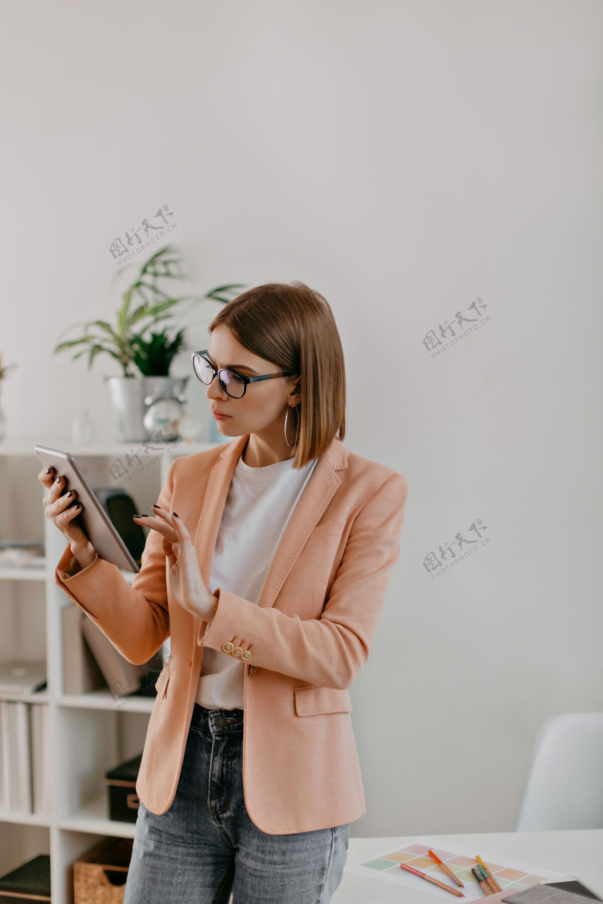 现代人在白色办公室工作的短发女士的快照穿着粉色夹克和白色t恤的女士若有所思地看着平板电脑办公室互联网财务