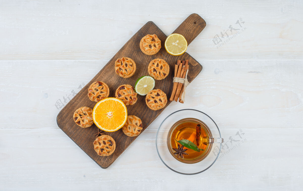 食物俯视图一个橘子 酸橙 饼干和肉桂在切菜板与一杯茶在白色的表面明星秋天饼干切刀