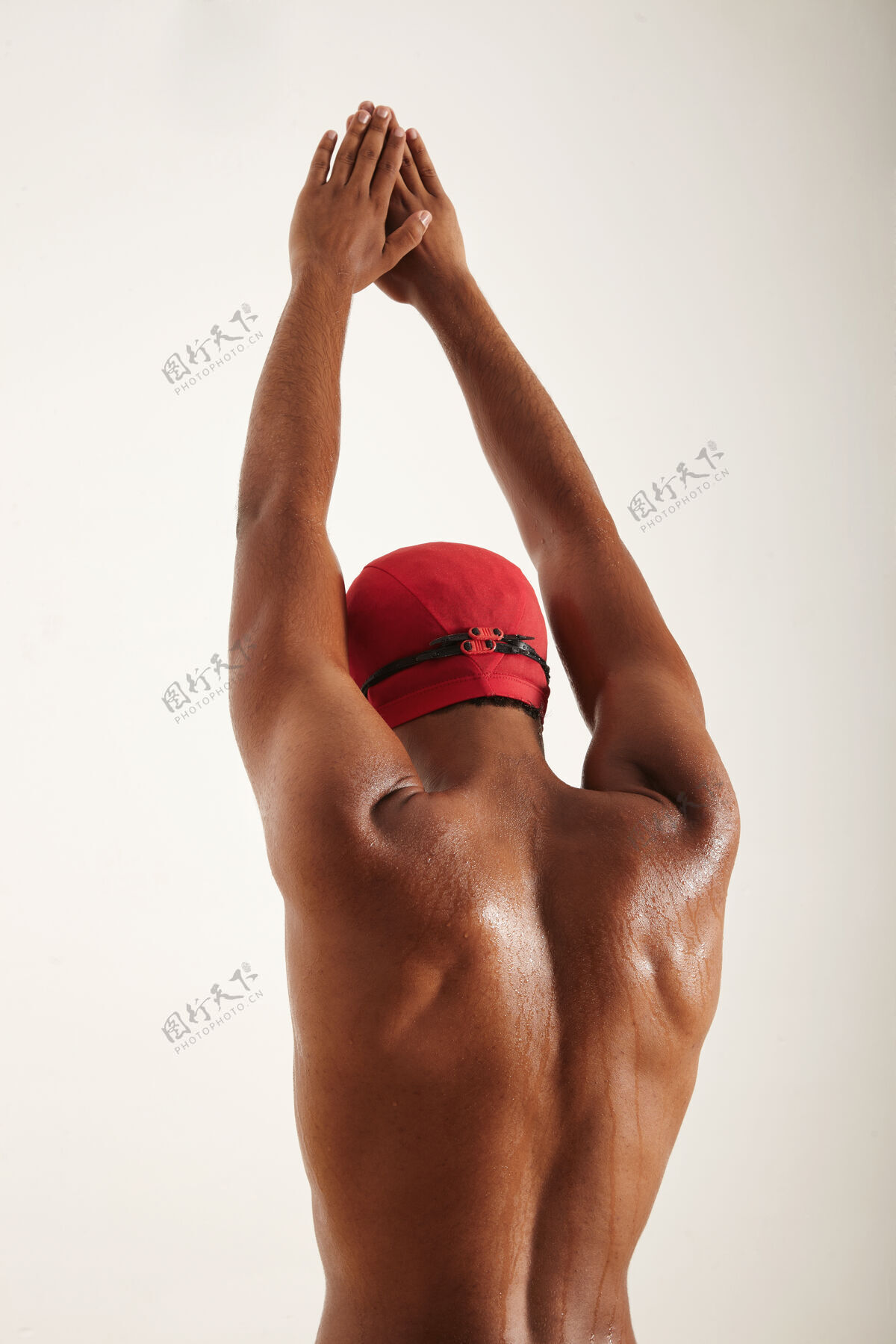 成人一个戴着红帽子和黑色护目镜的肌肉发达的非裔美国游泳运动员的背部和手臂 双臂伸向空中 准备在白色的水面上孤立地潜水人娱乐运动员