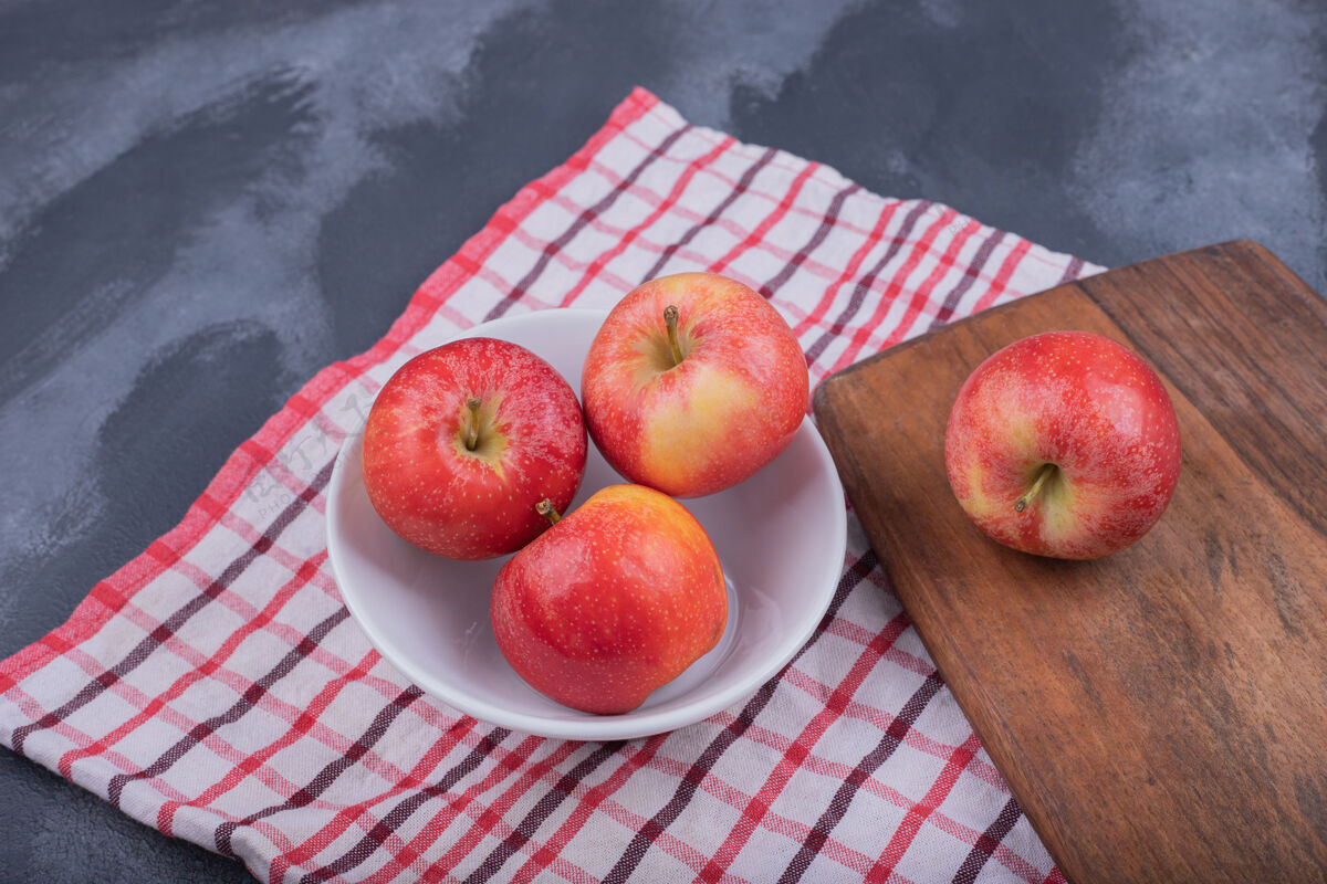 红的白盘子里有四个熟的 新鲜的苹果苹果木头毛巾