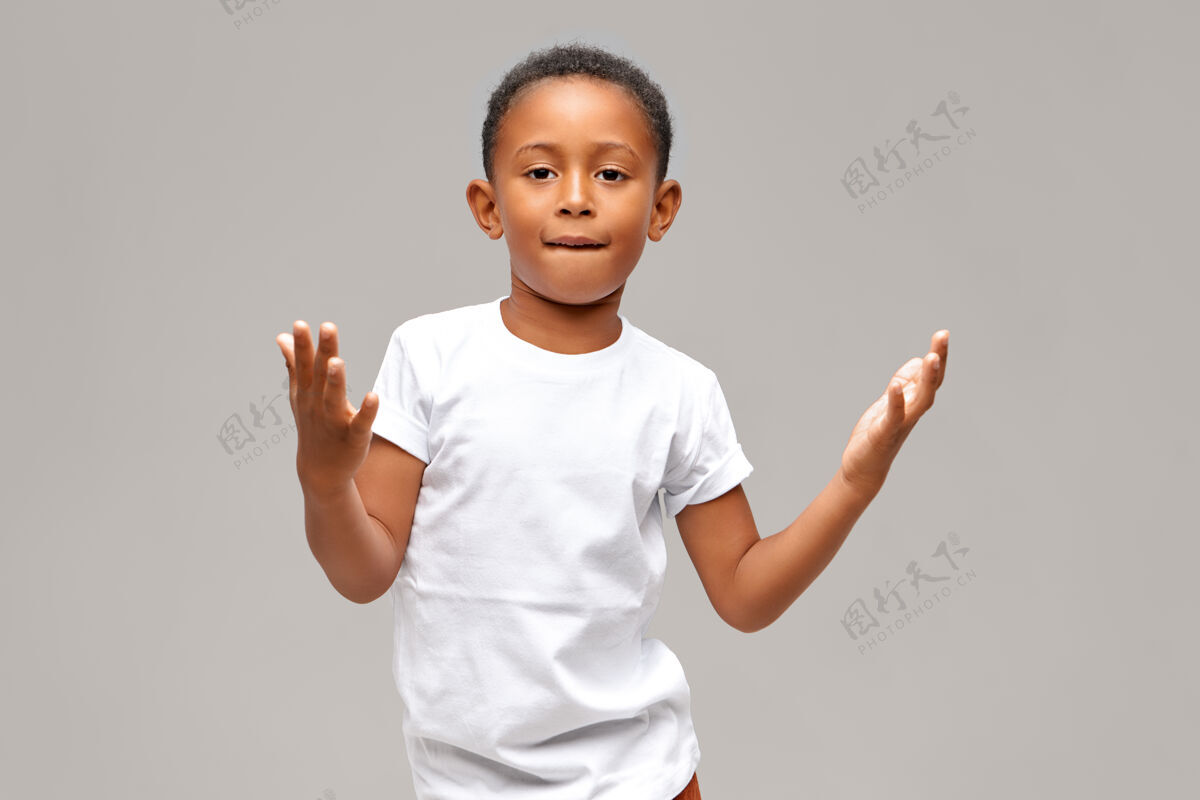 快乐酷酷可爱的非洲裔美国男孩的肖像 穿着休闲的白色t恤 有自信的面部表情 用手做一些手势 咬下唇孩子和生活方式的概念帅气非洲男孩