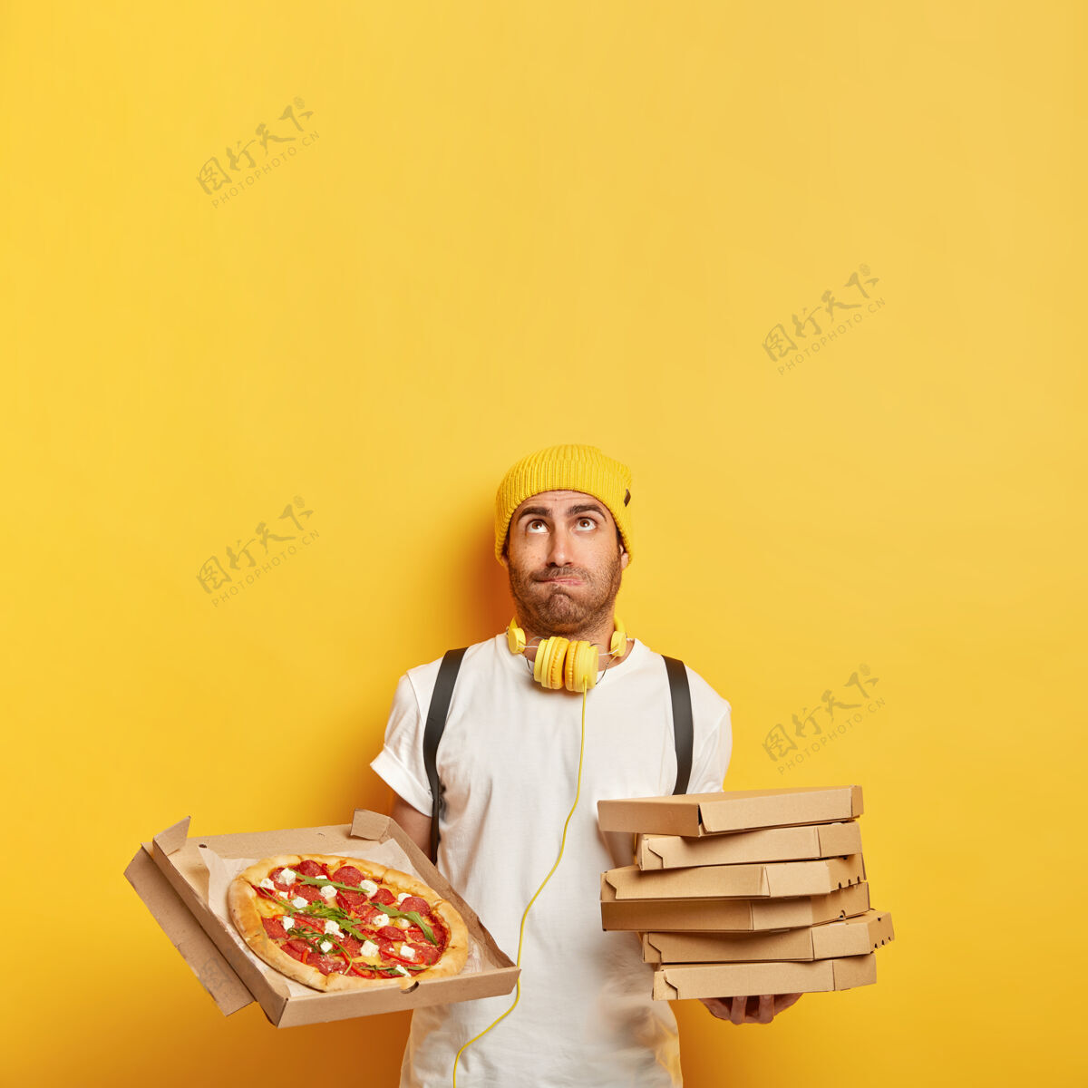 人送货员为客户带来纸板披萨盒 向上看 戴黄色帽子 穿白色t恤 工作运送快餐 隔离在黄色墙上 为您的推广复制空间站立职业集装箱
