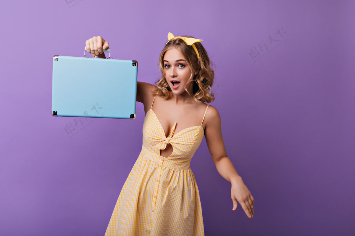 女性漂亮苗条的皮肤晒黑的女士拿着手提箱摆姿势室内的快乐金发女孩的肖像 蓝色的手提箱女人金发包