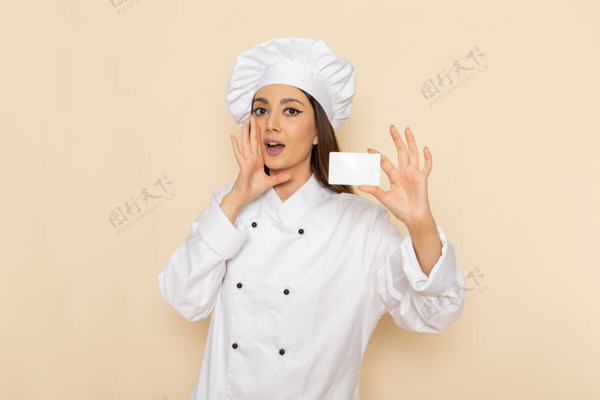 工人身穿白色厨师服的年轻女厨师的正面图 在浅白的墙上举着白色的牌子烹饪举行人