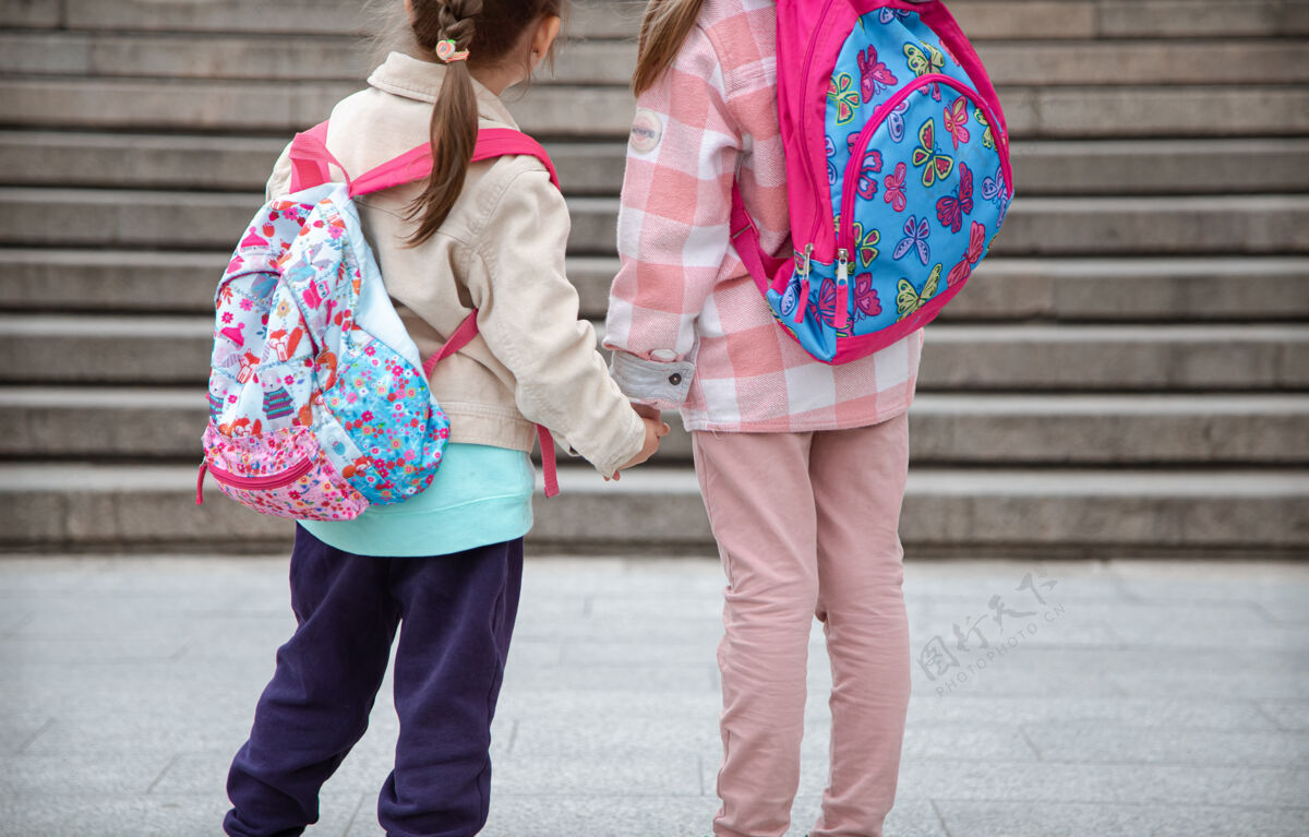 台阶两个背着漂亮背包的小女孩一起上学 手拉手 近距离接触童年友谊的概念姐妹小学生女孩