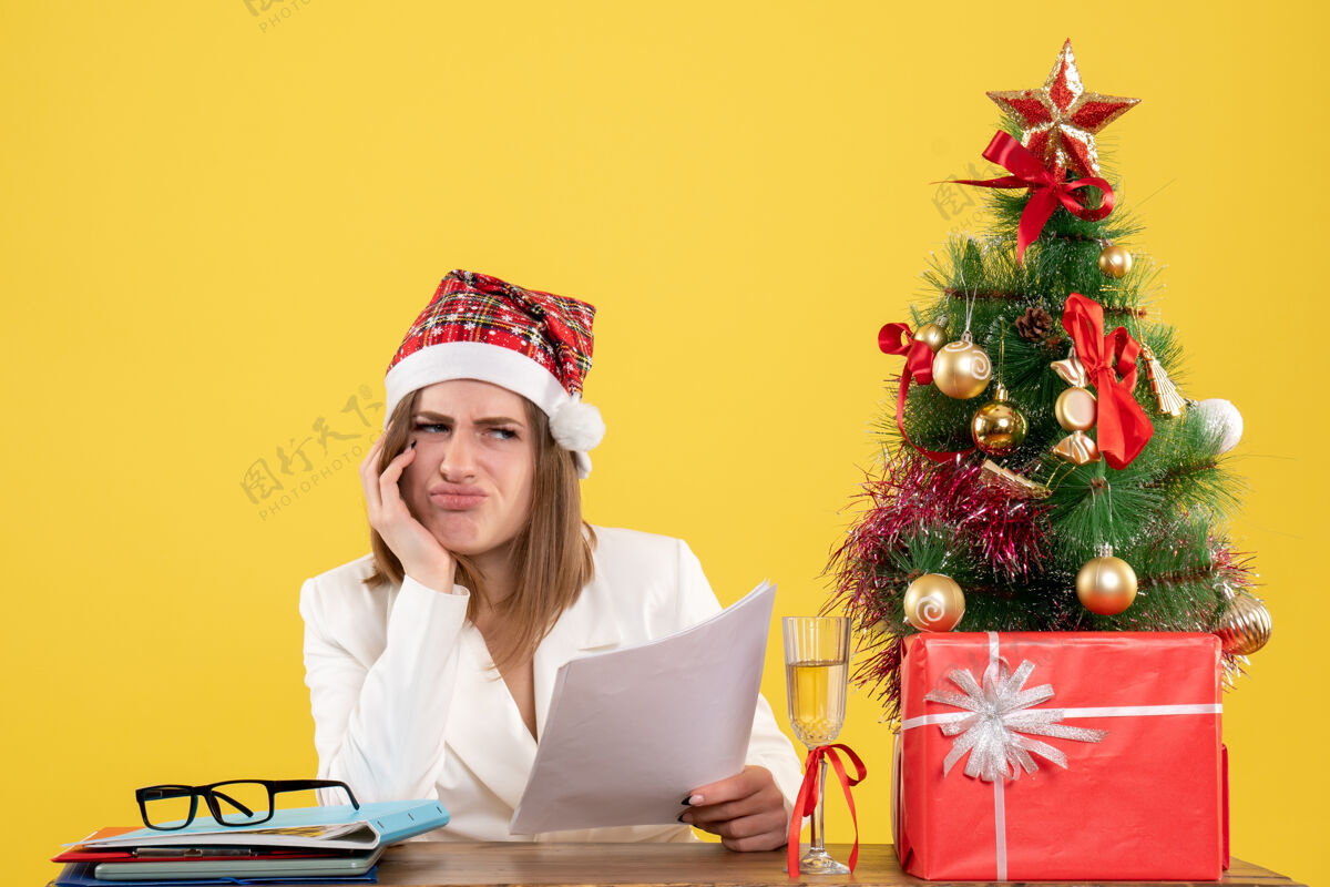 办公室前视图女医生坐在圣诞礼物拿着文件无聊的黄色背景微笑人无聊