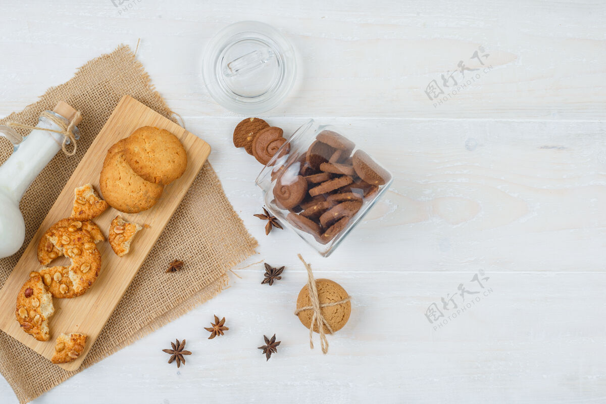 卡路里俯视图：棕色饼干放在玻璃罐里 还有一罐牛奶 饼干放在砧板上 白色表面有一个袋子曲奇自制堆栈