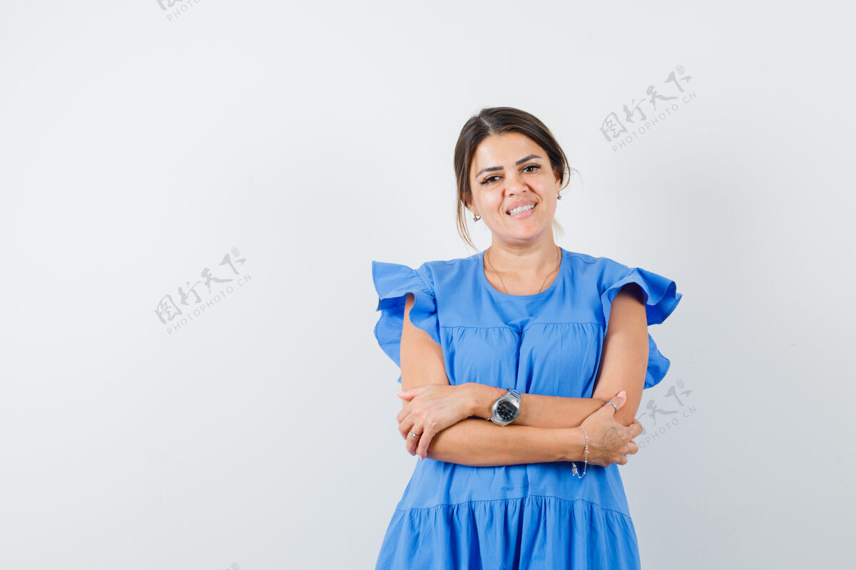 人年轻女子交叉着双臂站在蓝色的裙子上 看上去很欢快交叉可爱微笑