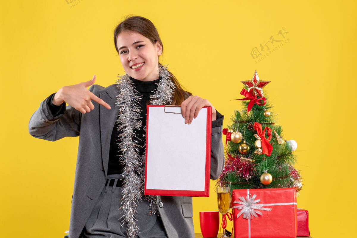 女孩前视图微笑的女孩展示文件站在圣诞树和鸡尾酒礼物附近人文件微笑