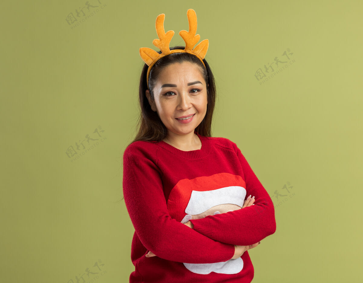 绿色穿着红色圣诞毛衣的年轻女子 戴着滑稽的鹿角边 双臂交叉 面带微笑女人胳膊新年