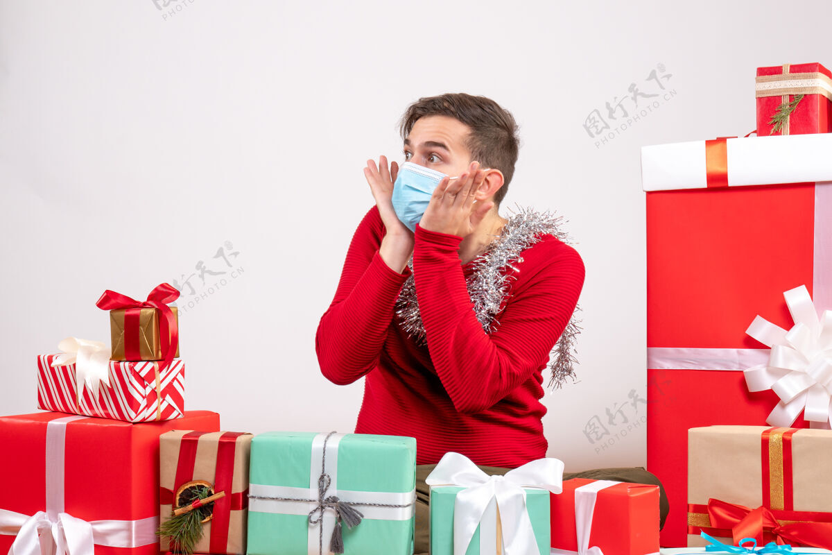 圣诞节前视图戴着面具的年轻人双手贴在脸颊上围坐着圣诞礼物面具放抱着