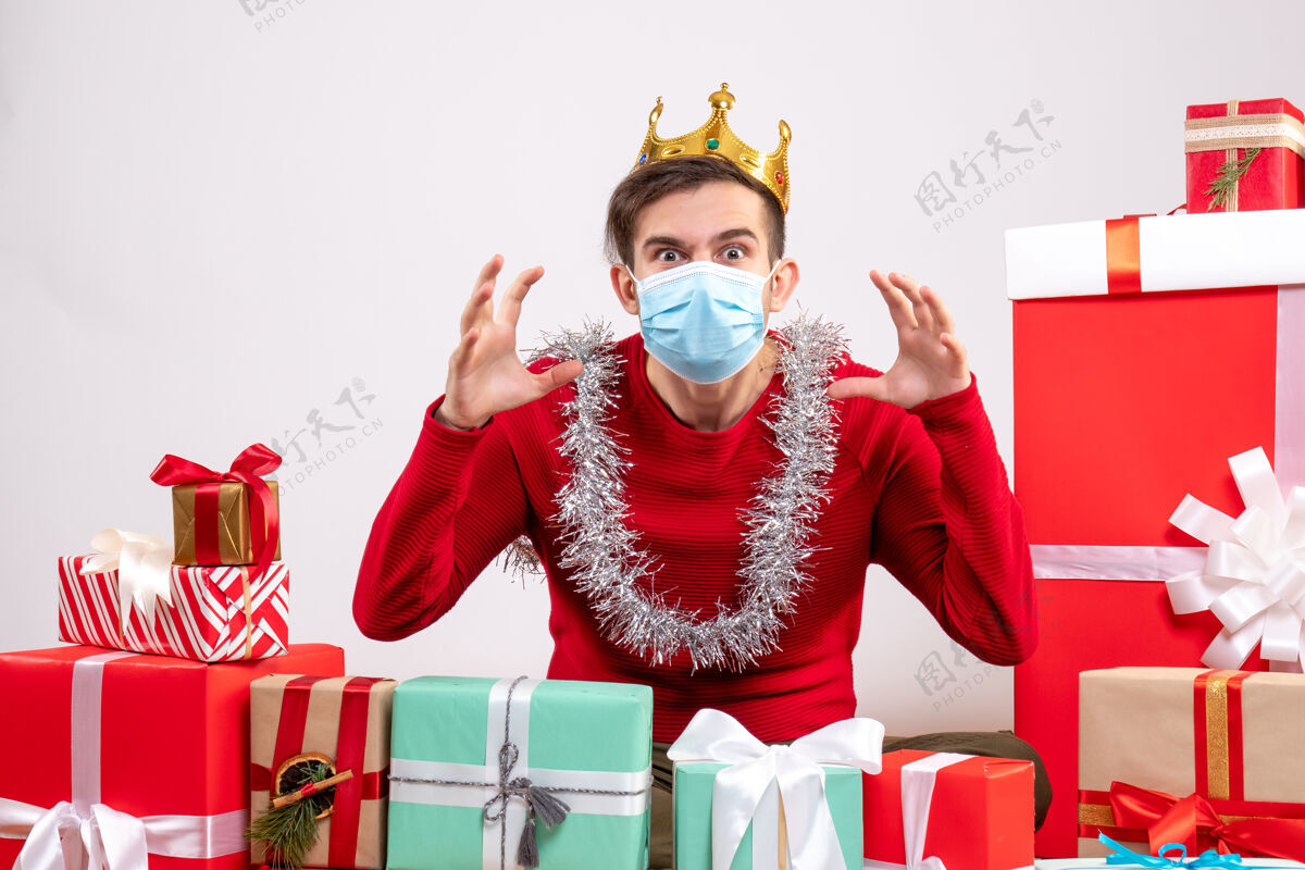 圣诞节正面图：戴着面具的年轻人坐在地上做着可怕的手势 圣诞礼物人服装恐怖