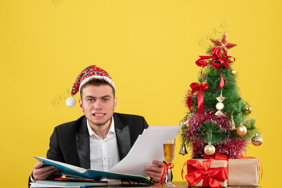 树前视图男性工人阅读文件周围的小圣诞树和一个黄色的礼物年份文件小