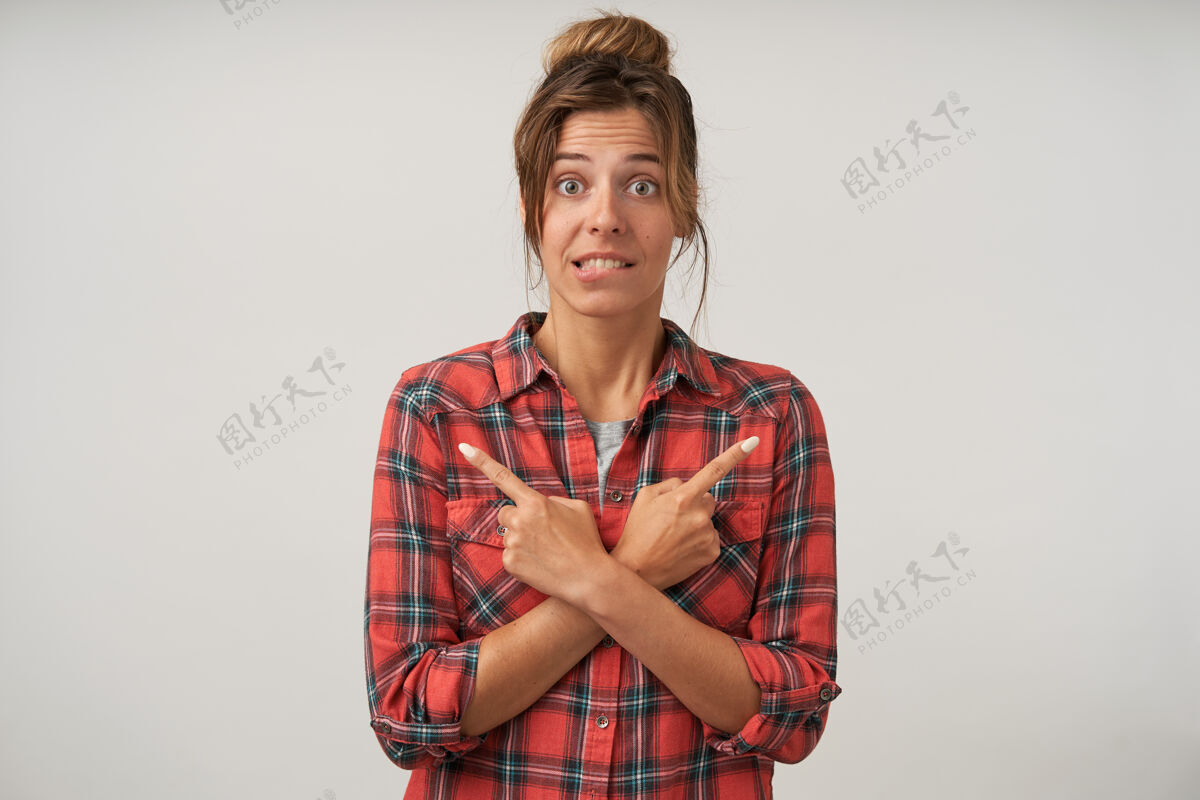 表情穿着格子衬衫的年轻漂亮女人的画像双手交叉放在胸前 食指指向不同的侧面 咬着臀部 收缩着前额收缩自然情绪