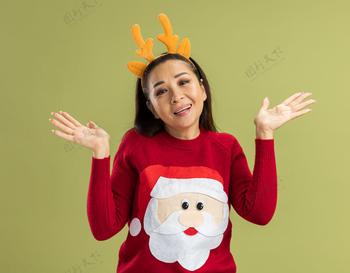 胳膊穿着红色圣诞毛衣的年轻女子 戴着滑稽的鹿角边 面带笑容 双臂高举红色年轻新年