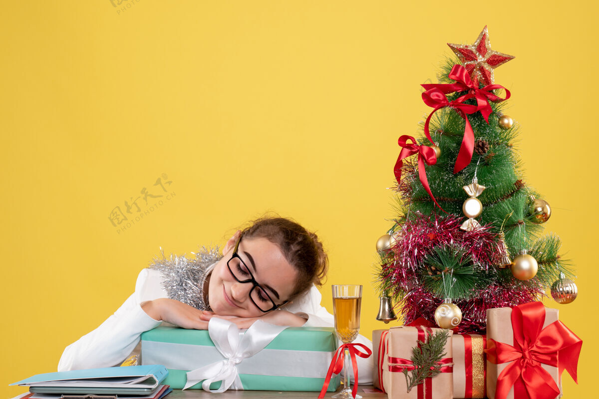 办公室正面图女医生围坐在黄色背景上的圣诞礼物和圣诞树旁花前面背景