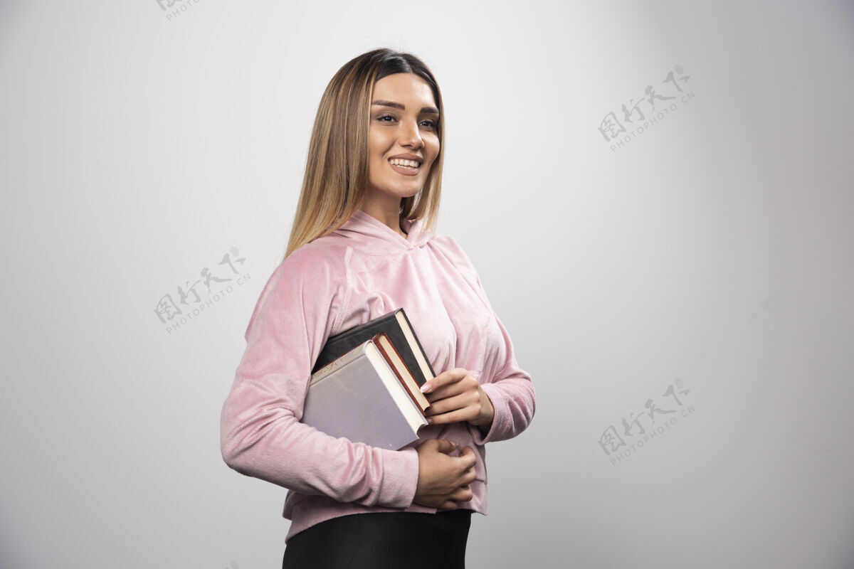 休闲一个穿着粉红色衬衫的女孩腋下夹着一堆书女人教育微笑