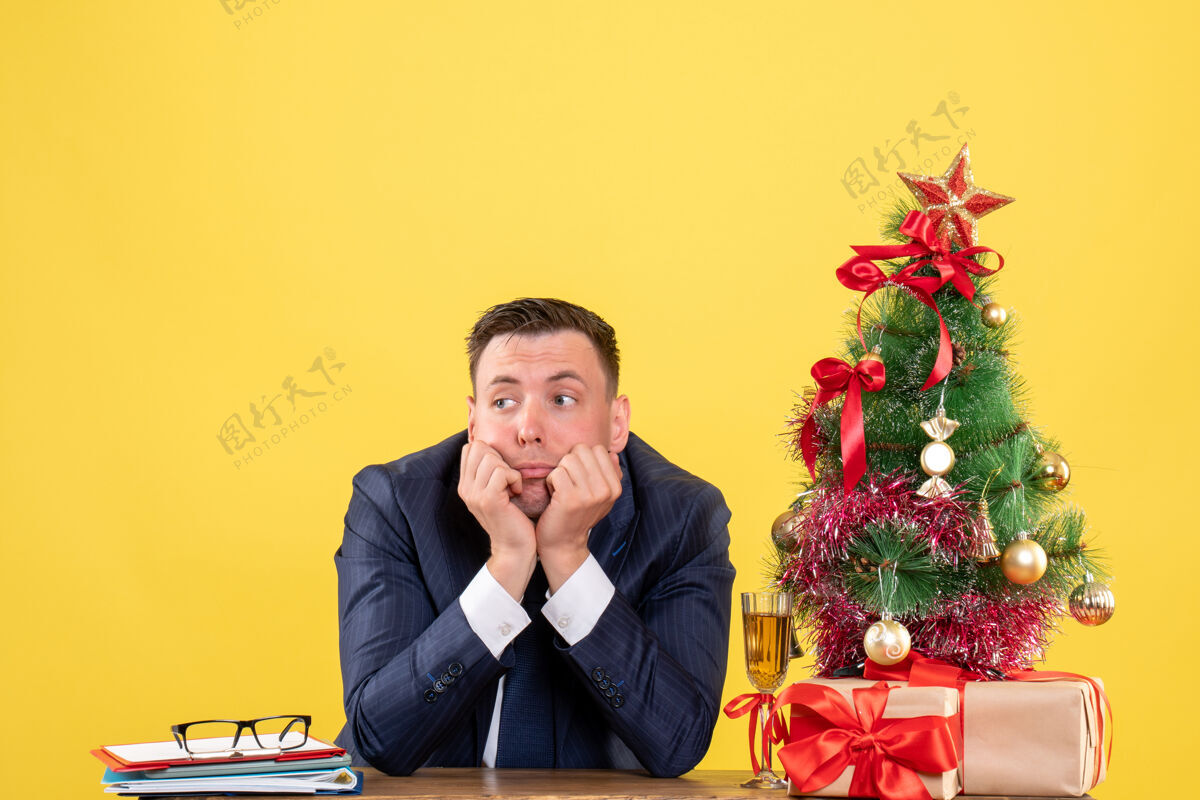 肖像前视图：体贴的男人坐在圣诞树旁的桌子旁 黄色的礼物体贴男人男性