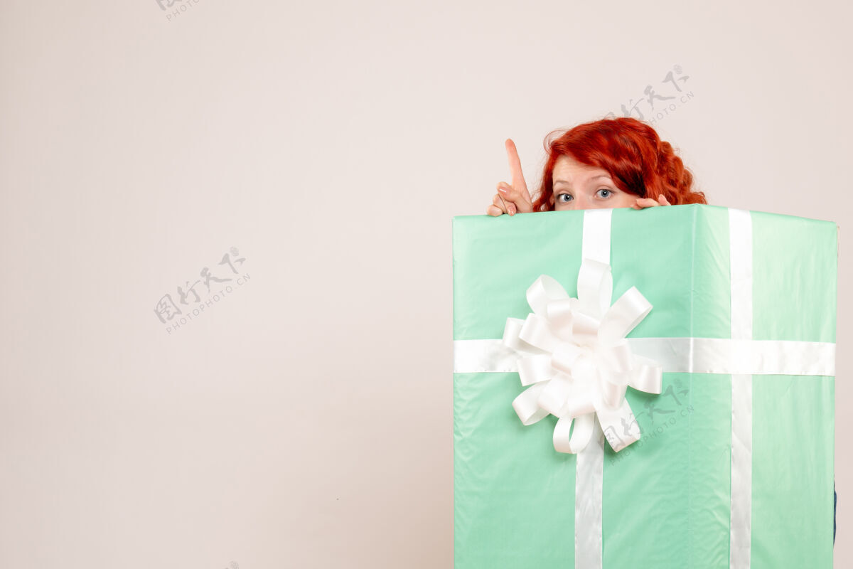 年轻女性前视图的年轻女子隐藏在圣诞礼物在白色的墙壁上里面圣诞快乐礼物