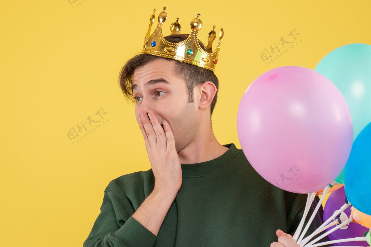 乐趣正面图戴着王冠和黑色面具的年轻人把手放在黄色的嘴巴上年轻人聚会气球