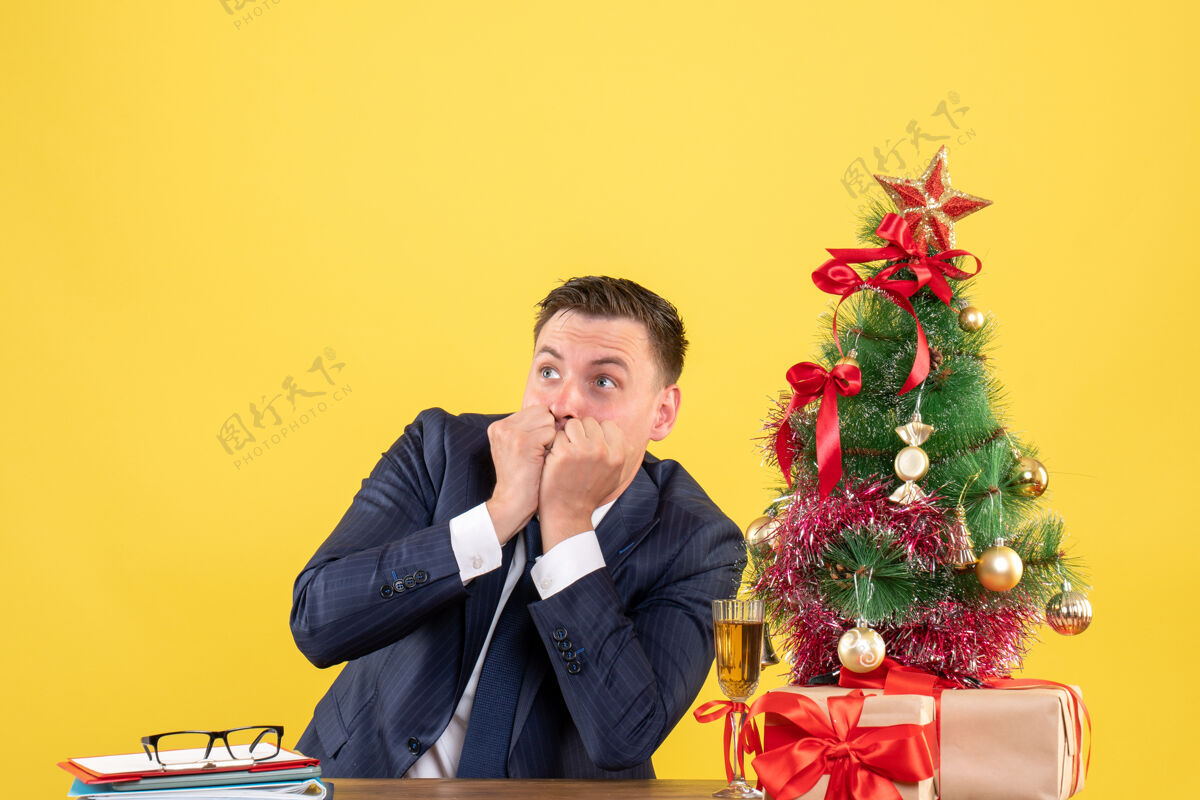 坐着前视图是一个好奇的人 他正在看圣诞树旁的桌子上坐着的东西和黄色的礼物人桌子好奇的