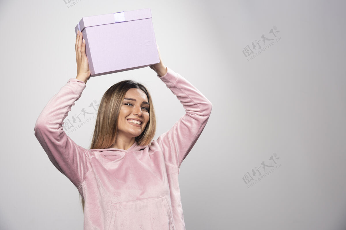 女士一位身穿粉色运动衫的金发女士头上举着一个礼盒 颤抖着礼物成人年轻