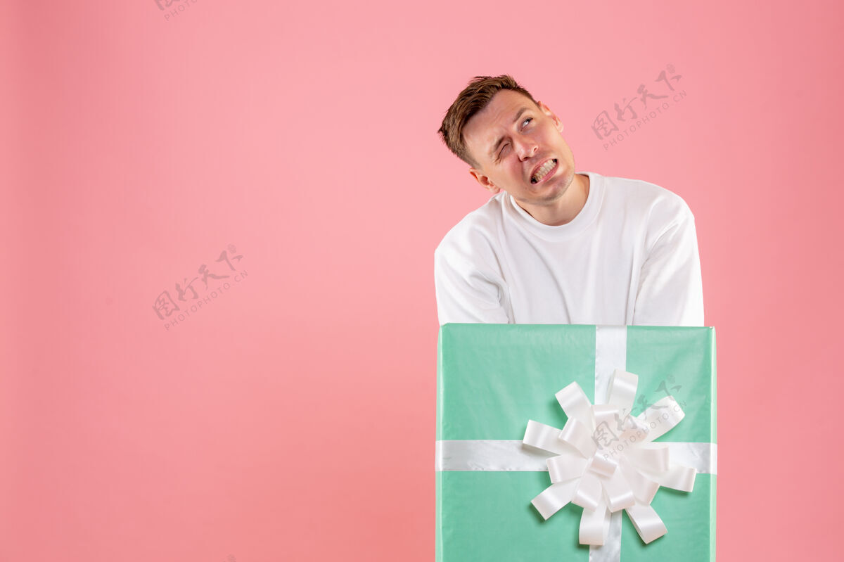 里面隐藏在粉红色墙上的礼物里面的年轻人的正面视图脸圣诞快乐庆祝