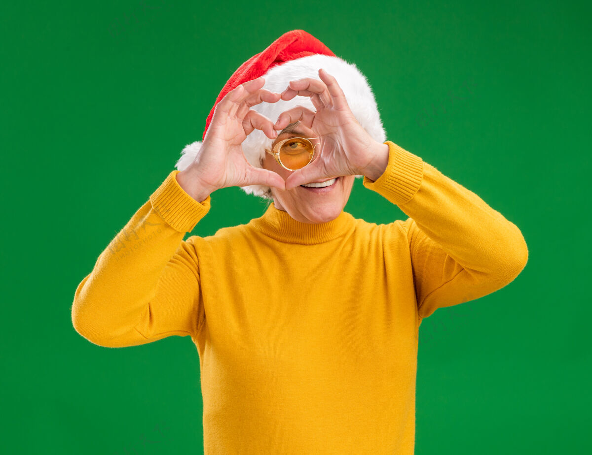 老人戴着太阳眼镜 戴着圣诞帽 微笑着的老妇人穿过心形标志标志绿色心