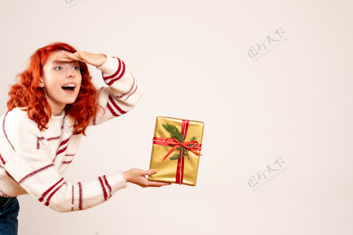 年轻白墙上挂着圣诞礼物的年轻女子的正视图庆祝微笑礼物