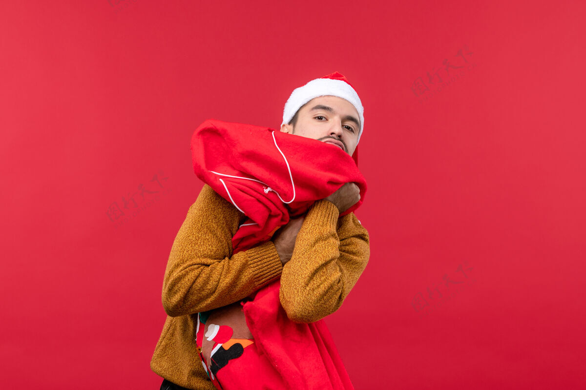 设备红墙上拿着礼物包的年轻人的正视图包圣诞节前面