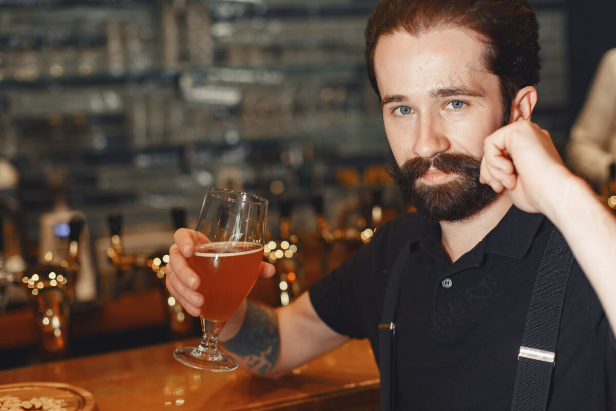 喝酒一个留着胡子的男人站在吧台旁 喝着酒杯里的酒成人酒吧男士