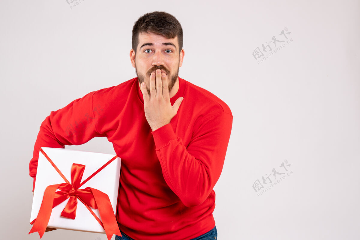 成人身穿红衫的年轻人在白色墙上的盒子里拿着圣诞礼物的正视图情感年轻人肖像