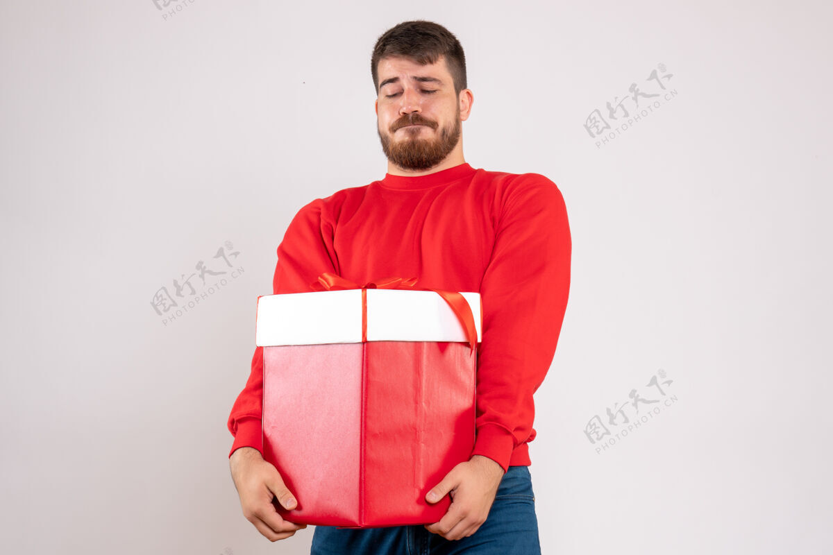 节日身穿红衫的年轻人在白色墙上的盒子里拿着圣诞礼物的正视图快乐圣诞节人