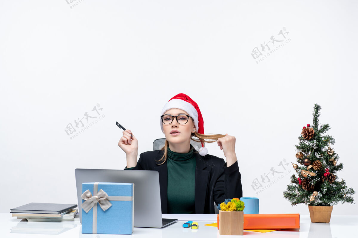 金发一个金发女郎拿着圣诞帽坐在桌子旁 手里拿着圣诞树和礼物圣诞老人圣诞老人坐着