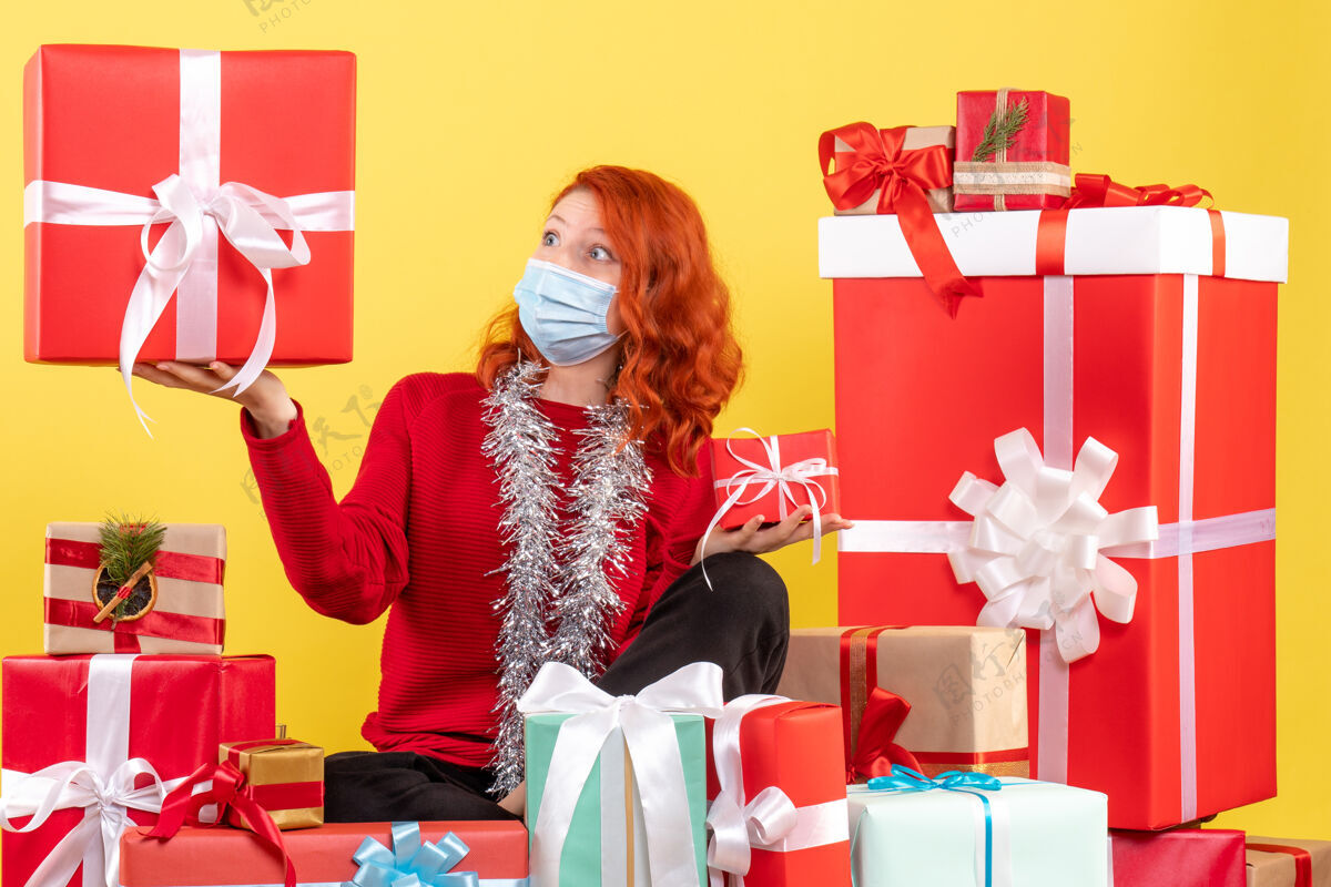 购物者坐在黄色墙壁上戴着面具的年轻女子的圣诞礼物前视图快乐Covid坐着