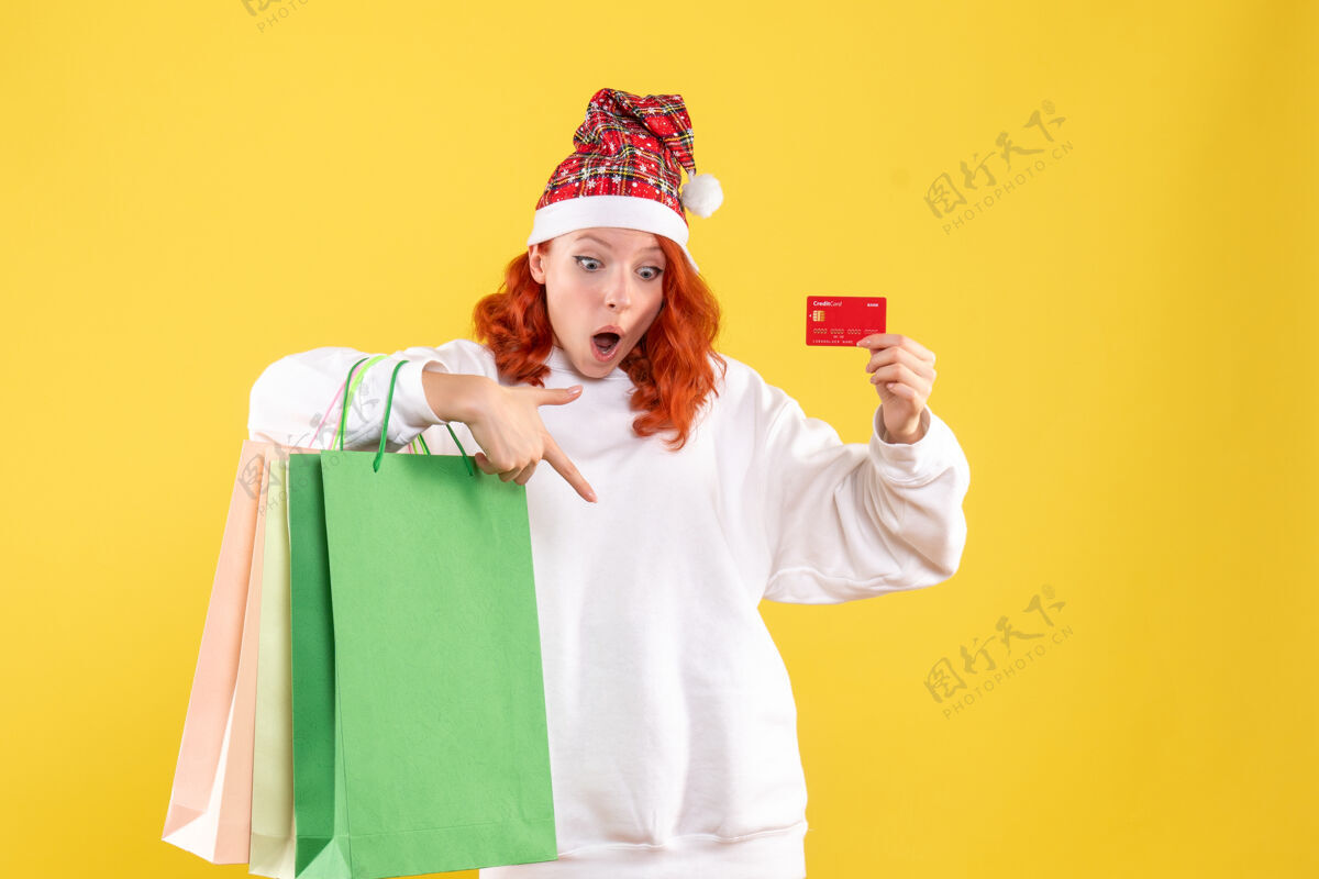 年轻女性黄墙上拿着购物包和银行卡的年轻女子的正视图肖像微笑人