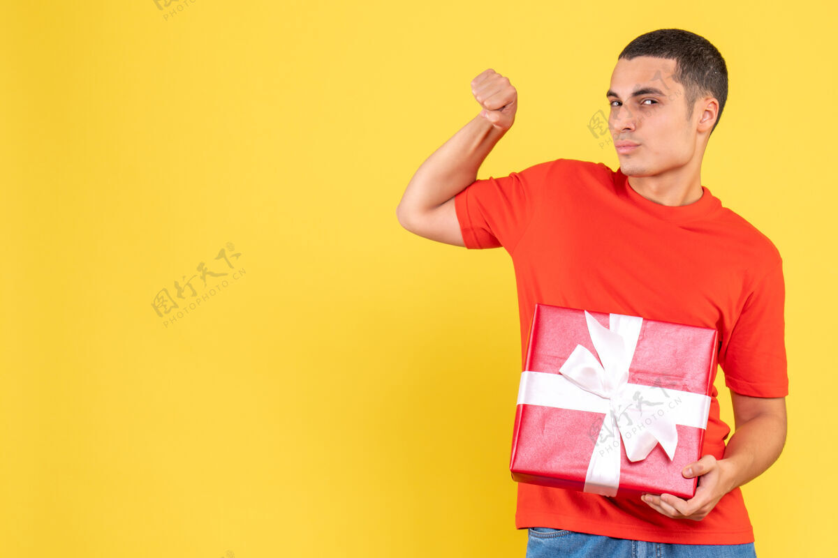 快乐黄色墙上年轻人拿着礼物的正面图年轻男性前面节日