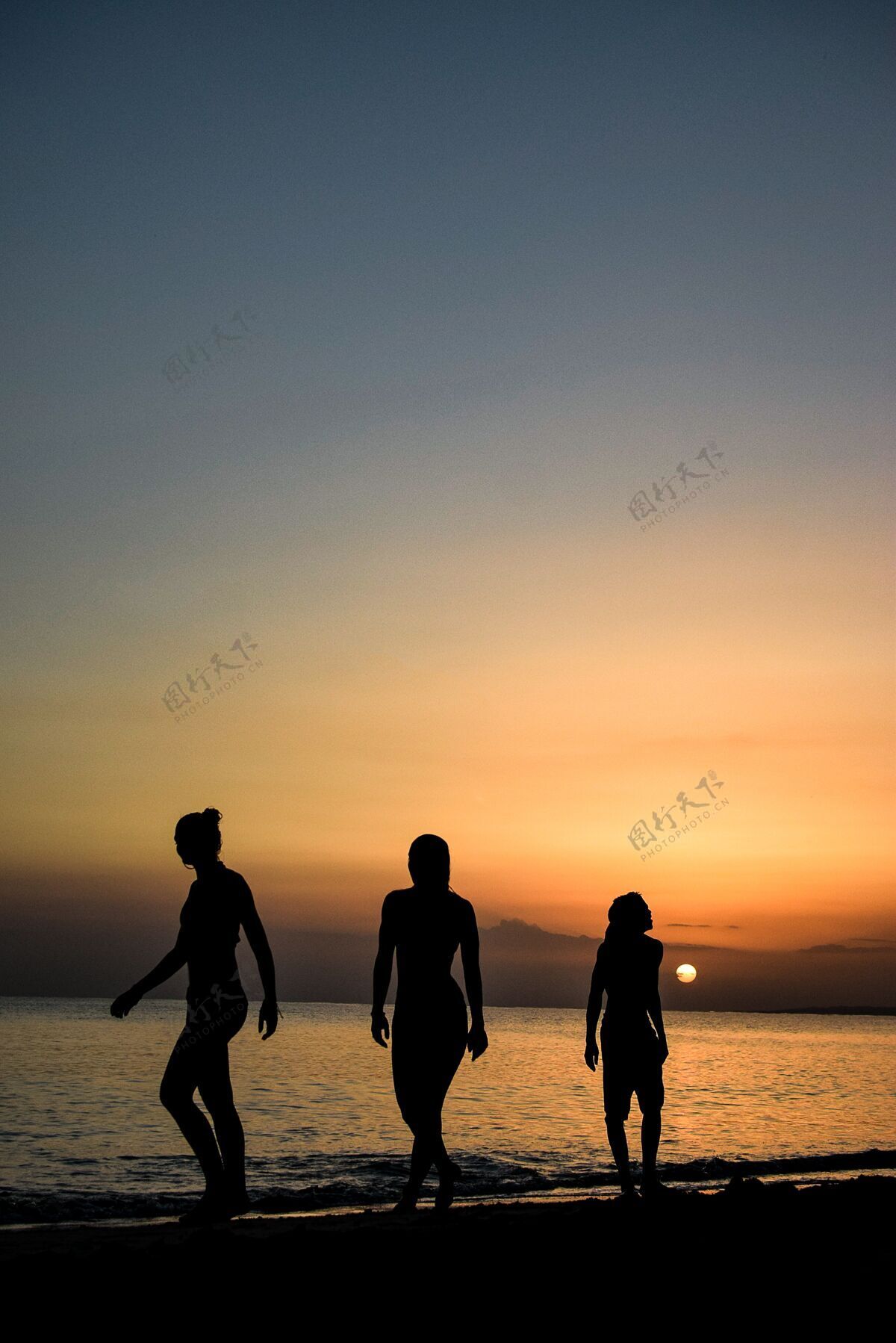 海滩垂直拍摄的人走在令人惊叹的日落下的海洋自然浪漫户外