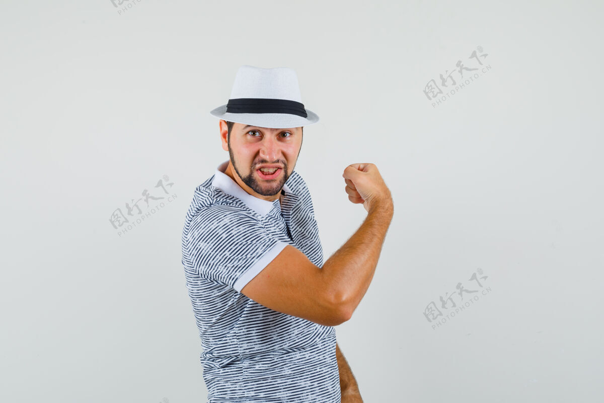 工作室穿着t恤 戴着帽子 展示手臂肌肉的年轻人 看上去很有力量前视图男人休闲成人