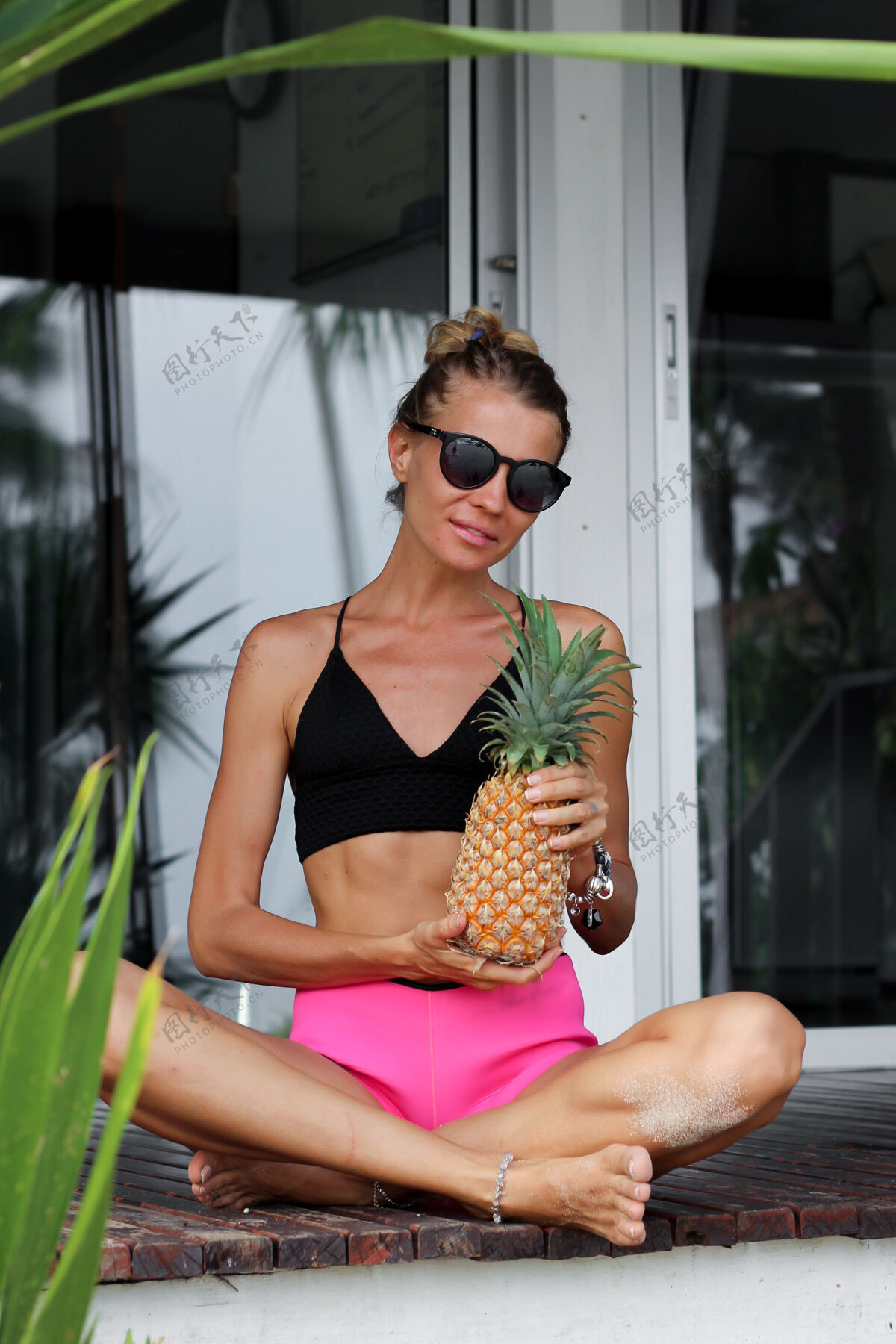 户外穿着黑色上衣粉色短裤的白种女人在热带别墅外抱着菠萝菠萝人人