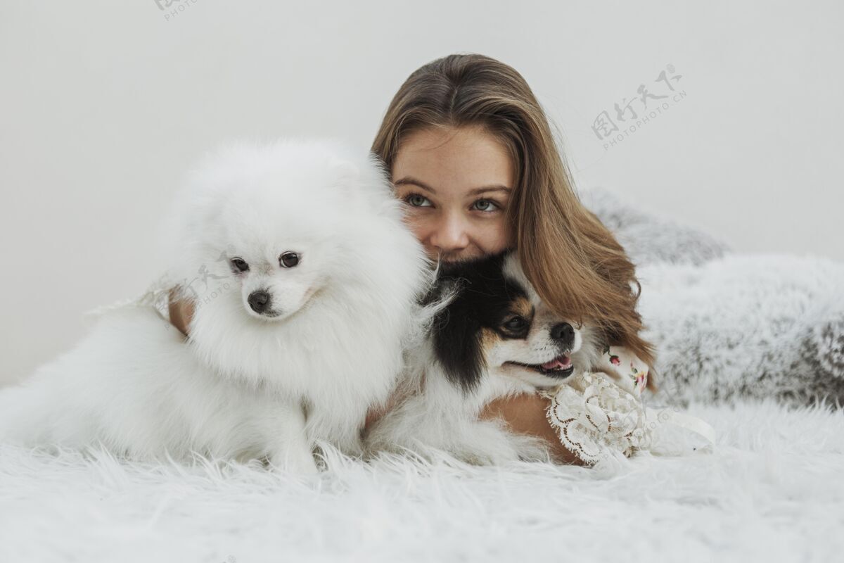 狗女孩和可爱的白色小狗坐在床上在一起年轻友谊