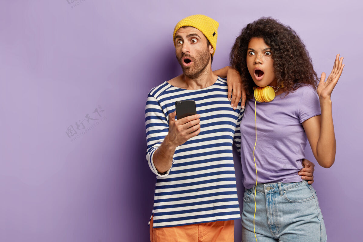 互联网室内拍摄的惊呆夫妻用手机查看新闻 凝视远方 看着可怕的一幕恐惧卷发害怕