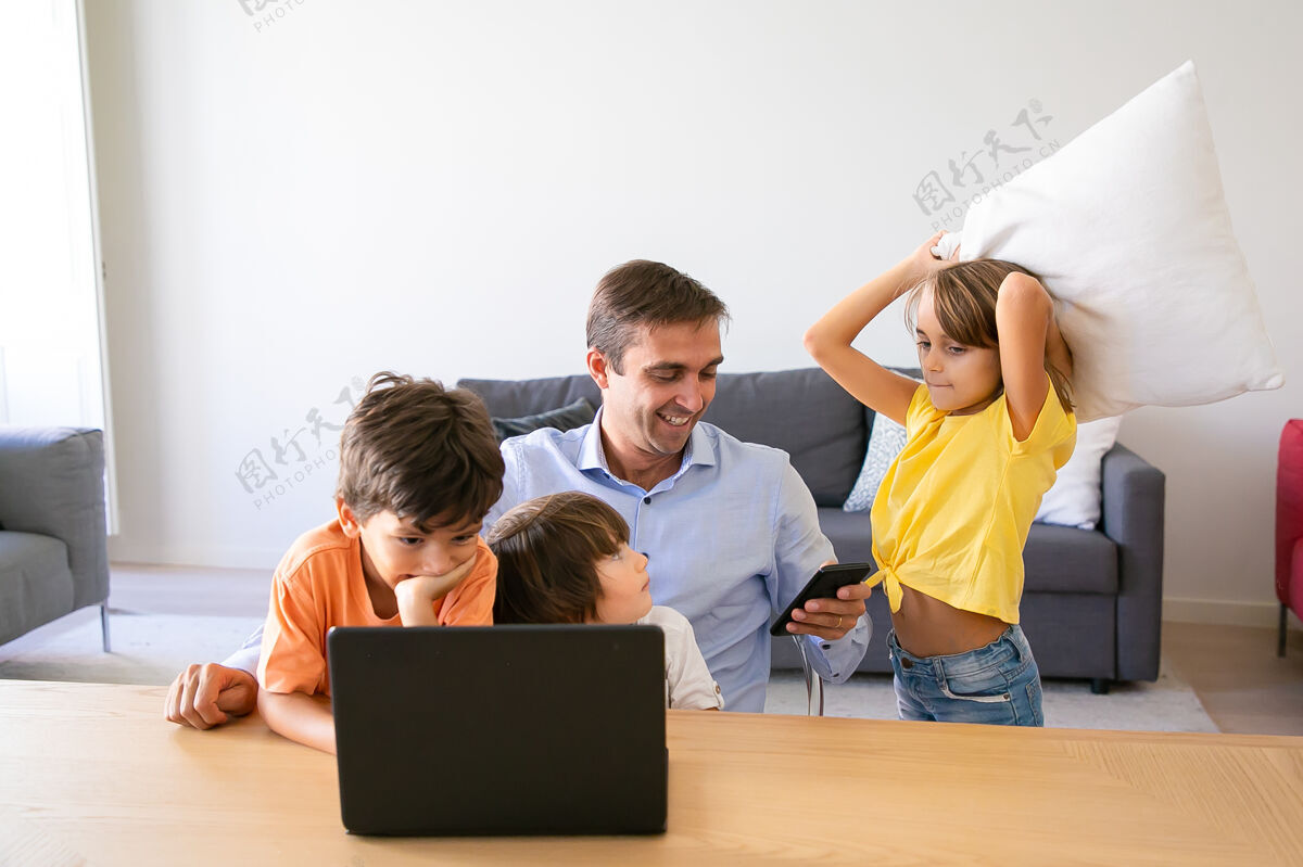 朋友快乐的爸爸用智能手机 坐在桌子旁 孩子们和他一起玩白人爸爸在家工作 用笔记本电脑 看孩子父亲 童年和数字技术的概念女儿房间儿子