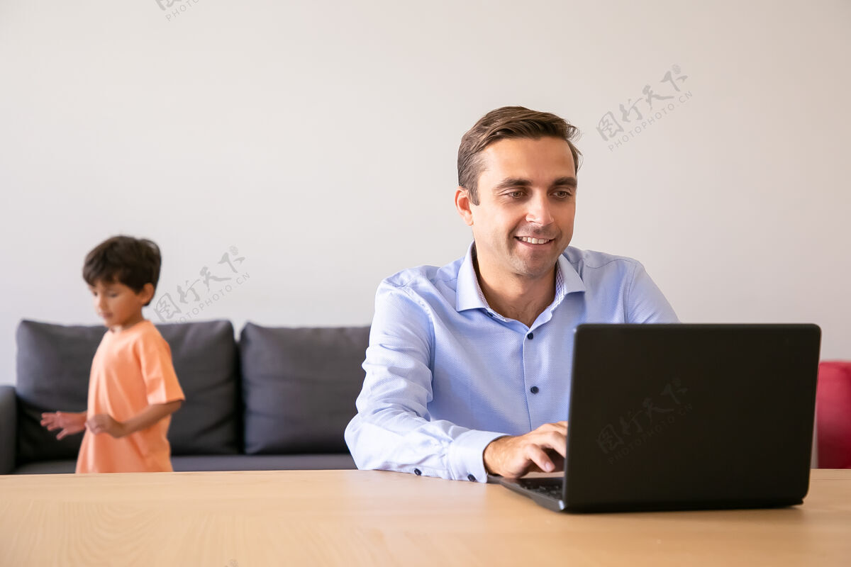 在线当男孩在他身边玩耍时 快乐的爸爸在网上浏览白人爸爸在家使用笔记本电脑和工作枕头室内站立