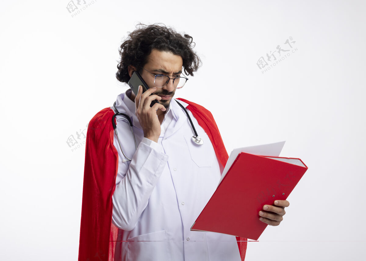 眼镜严肃的年轻白种人超级英雄 戴着眼镜 穿着医生制服 披着红色斗篷 脖子上戴着听诊器 一边打电话一边看文件夹里的复印件制服文件看