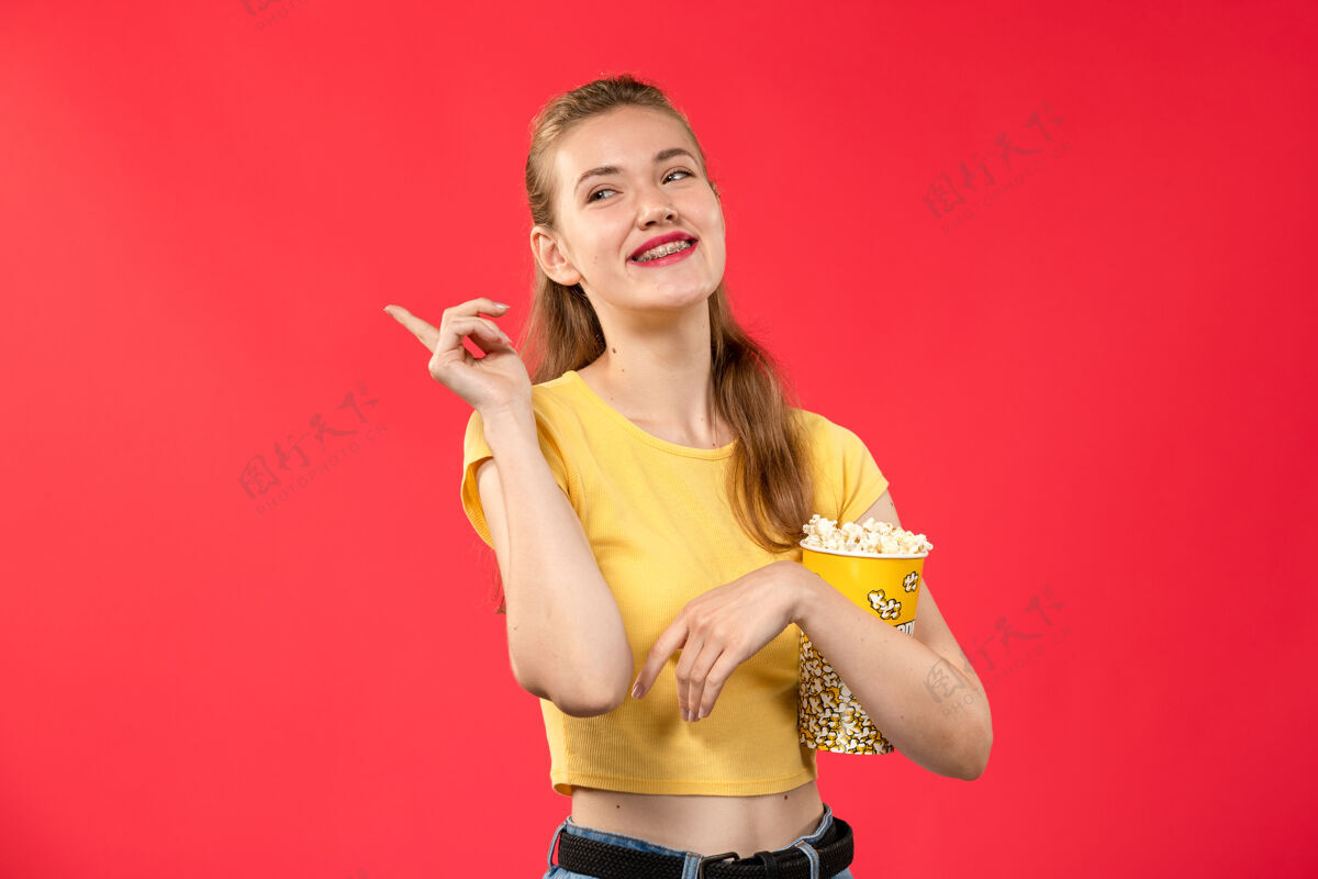 观点正面图年轻女性在电影院拿着爆米花包 笑着看淡红墙影院的电影笑身体成人